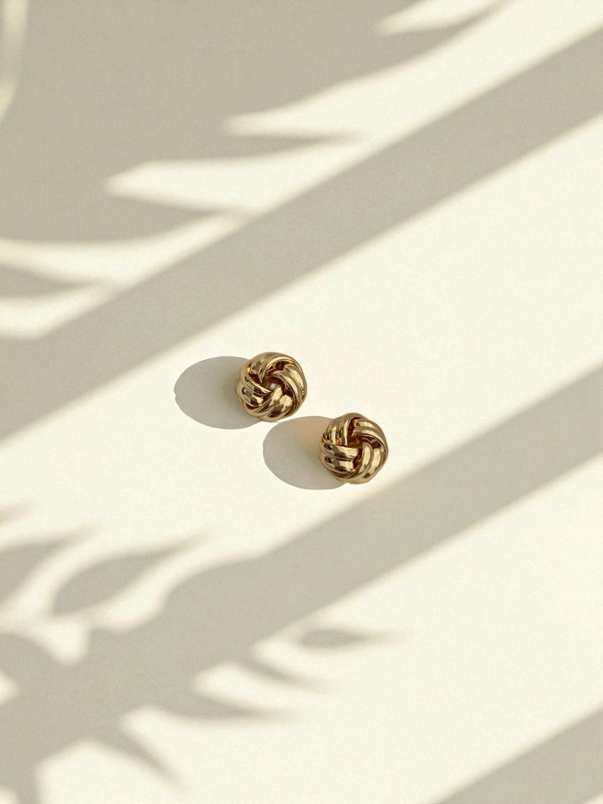 Gold knot earrings on a light surface with shadows