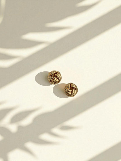 Gold knot earrings on a light surface with shadows