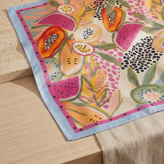 Colorful silk scarf with tropical fruit design on a wooden surface