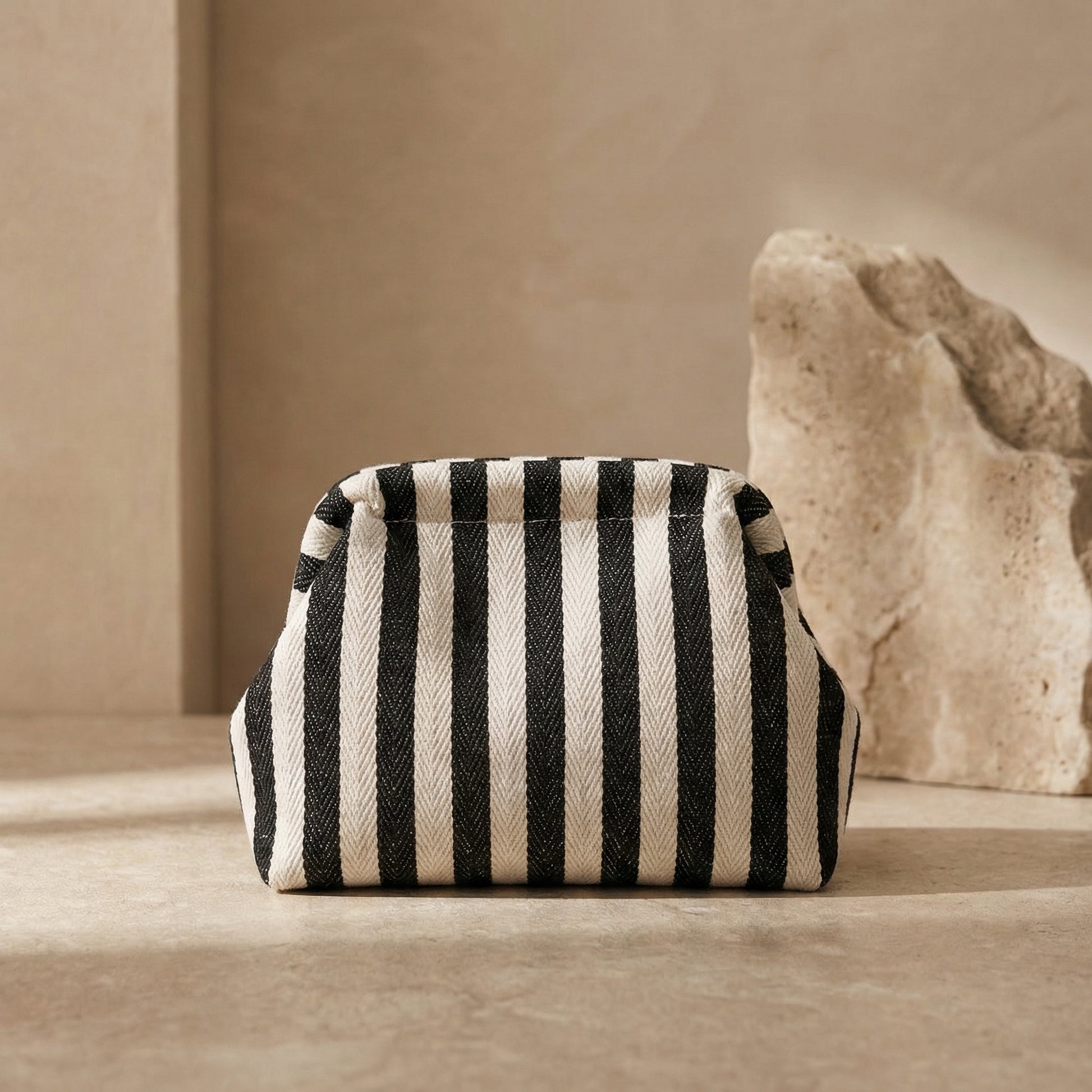 Black and white striped pouch on a beige surface with a stone-like object in the background