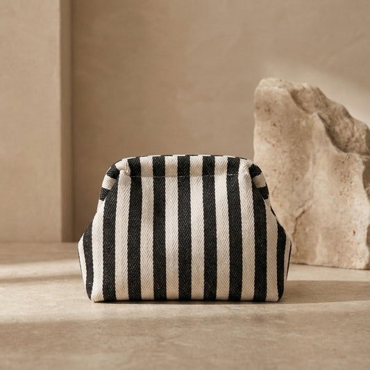 Black and white striped pouch on a beige surface with a stone-like object in the background