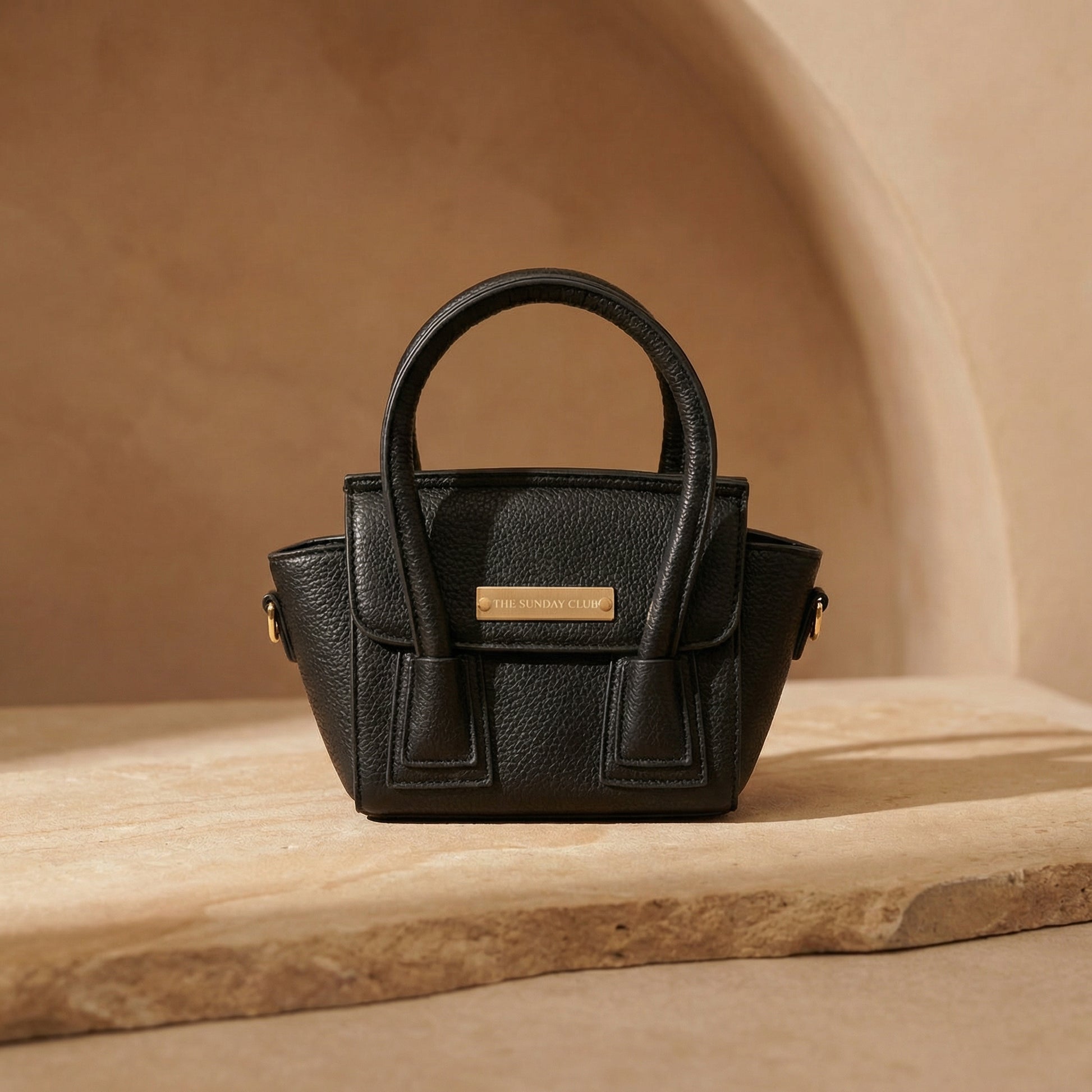 Black handbag with a gold tag on a wooden surface and beige background